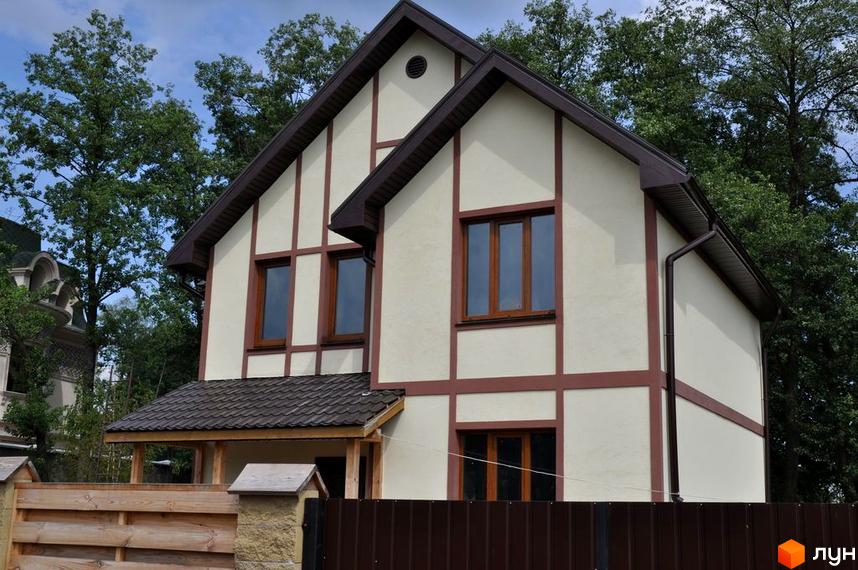 Двоповерховий будинок з коричневими вікнами та оздобленням на фасаді. Перед будинком розташований дерев'яний паркан та зелені насадження.