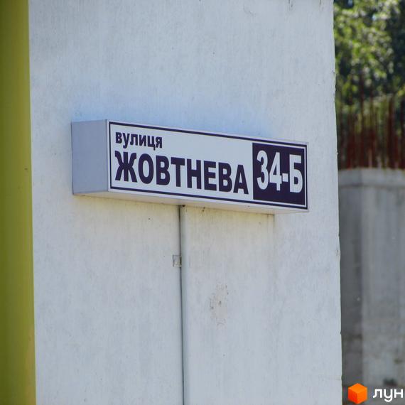 Вулична табличка з назвою вулиці Жовтнева, 34-Б. Зовнішній вигляд фасаду будівлі та прибудинкової території.