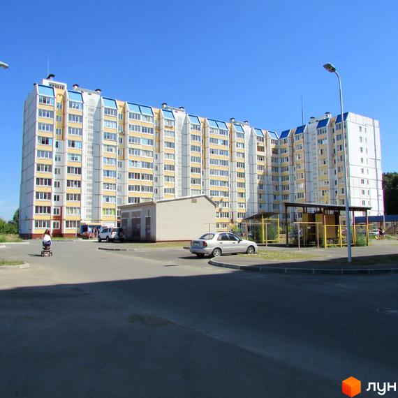 Житловий комплекс на вул. Жовтнева, 34б. Багатоповерховий будинок з жовтими та білими фасадами, синіми дахами. Прибудинкова територія з автомобілями та дитячою коляскою.