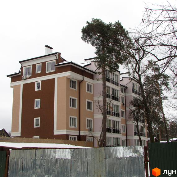 Зовнішній вигляд багатоквартирного будинку ЖК Київський дворик з коричневими та бежевими фасадами. Навколо будівлі видно дерева та паркан.