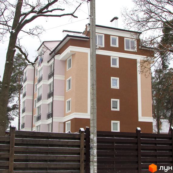 Житловий комплекс Київський дворик. Багатоповерховий будинок з коричневими та бежевими фасадами, балконами та вікнами. На передньому плані дерев'яний паркан.