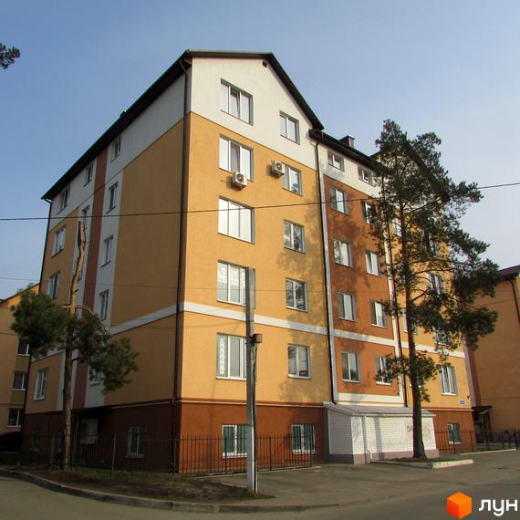 Зовнішній вигляд багатоповерхового будинку з жовто-коричневим фасадом та білими елементами. Навколо будинку зелені насадження та паркан.