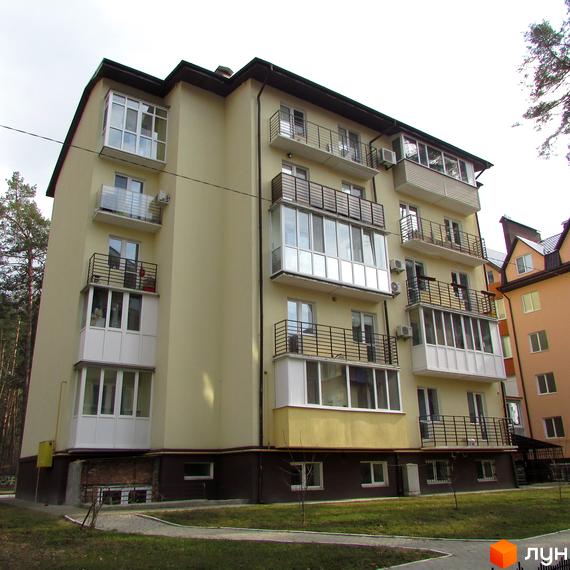 Клубний будинок „10-а лінія“ з жовтим фасадом, балконами та скляними лоджіями. Навколо будинку зелена галявина та доріжки.