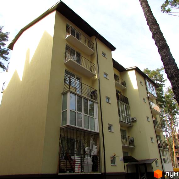 Клубний будинок „10-а лінія“ з балконами та вікнами, фасади світло-жовтого кольору. Навколо будинку дерева та блакитне небо.