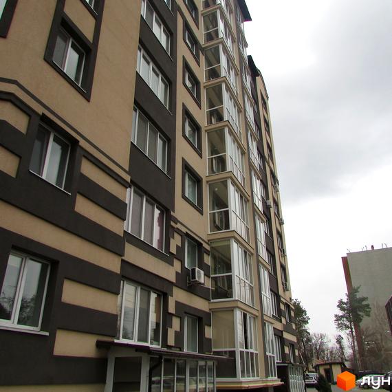 Зовнішній вигляд новобудови ЖК Котляревського з коричневими та бежевими фасадами, скляними балконами та великими вікнами. Навколо будинку видно дерева та сіре небо.