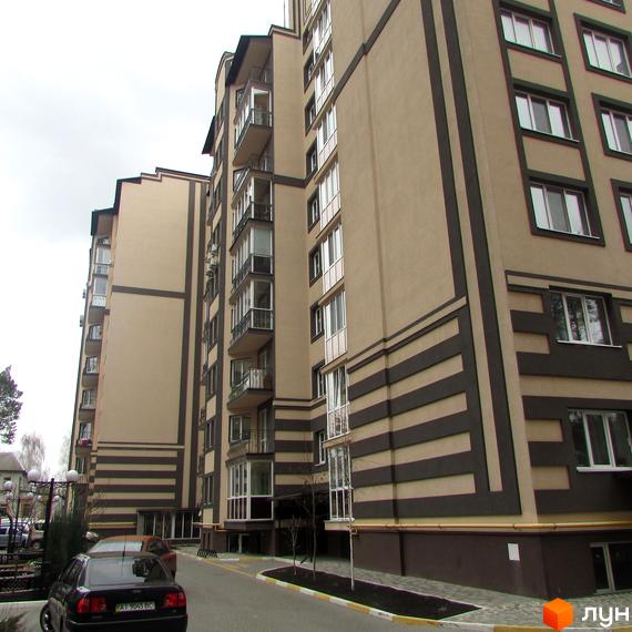 Зовнішній вигляд новобудови ЖК Котляревського з коричневими та бежевими фасадами, балконами та вікнами. Прибудинкова територія з дорогою та припаркованими автомобілями.