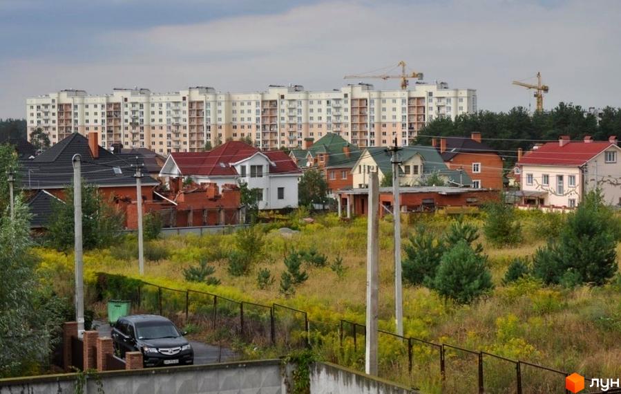 Житловий комплекс з таунхаусами та багатоповерховими будинками. На передньому плані зелена прибудинкова територія з рослинністю та парканом.