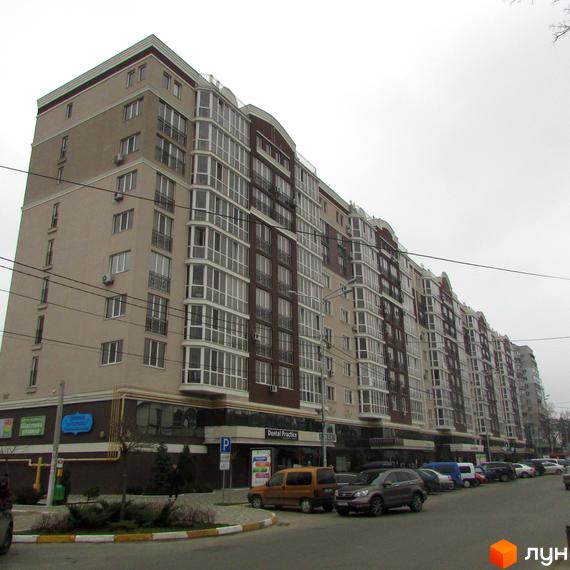 Зовнішній вигляд новобудови ЖК Соборний з численними балконами та вікнами. Навколо будинку розташовані припарковані автомобілі та елементи міської інфраструктури.