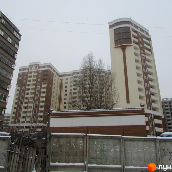 Житловий комплекс Palladium складається з висотних корпусів з коричнево-бежевими фасадами та скляним еркером. Перед будинком видно бетонний паркан.