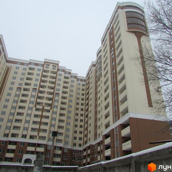 Житловий комплекс Palladium - висотна новобудова з балконами та панорамними вікнами. Зовнішній вигляд будівлі виконаний в бежевих та коричневих тонах. Навколо комплексу видно дерева та паркан.