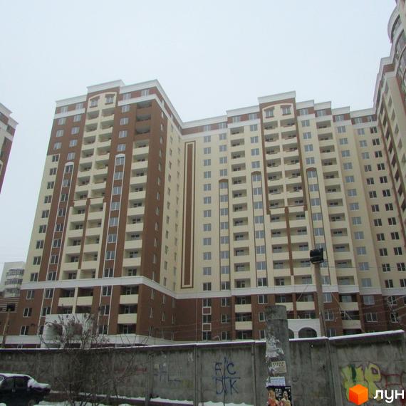 Житловий комплекс Palladium - багатоповерховий будинок з коричневими та світло-бежевими фасадами, балконами та великою кількістю вікон. На передньому плані видно бетонний паркан та дерева.