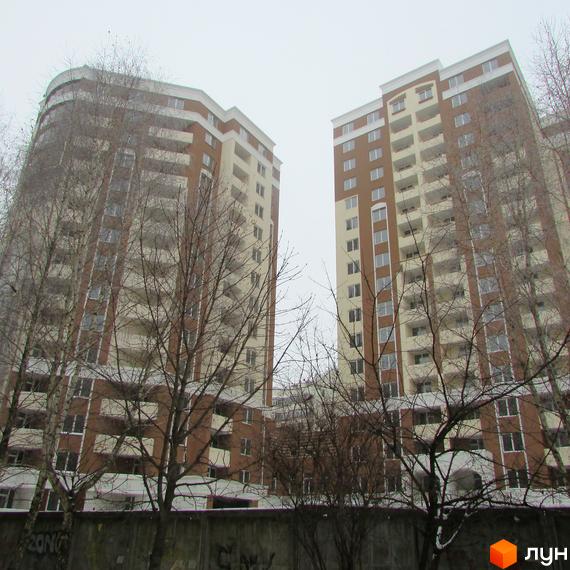 Житловий комплекс Palladium: двоповерхові будинки з коричнево-бежевими фасадами та балконами. Навколо будівель ростуть дерева без листя.