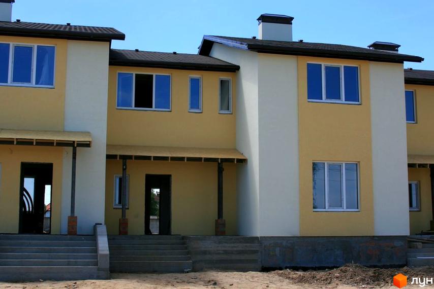 Зовнішній вигляд будинку житлового комплексу. Фасад будівлі з вікнами та вхідними дверима, перед будинком сходи та невеликий газон.