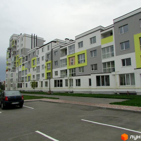 Новобудова ЖК Сан Сіті з яскравими зеленими та сірими акцентами на фасаді. Перед будинком розташований паркінг та зелена зона.