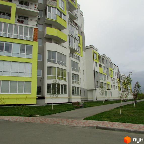 Житловий комплекс Сан Сіті – це сучасна новобудова з яскравим фасадом та доглянутою прибудинковою територією. На фото видно зелену зону з доріжками та лавками.