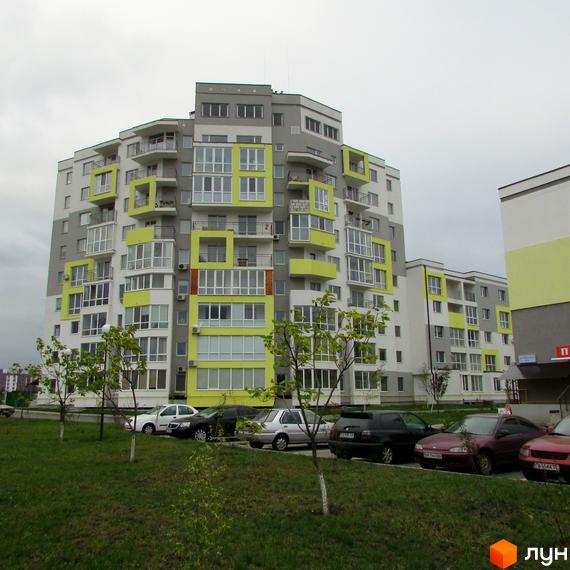 Житловий комплекс Сан Сіті – багатоповерховий будинок з яскравими зеленими та сірими фасадами. Перед будинком розташована парковка з автомобілями та зелена галявина.