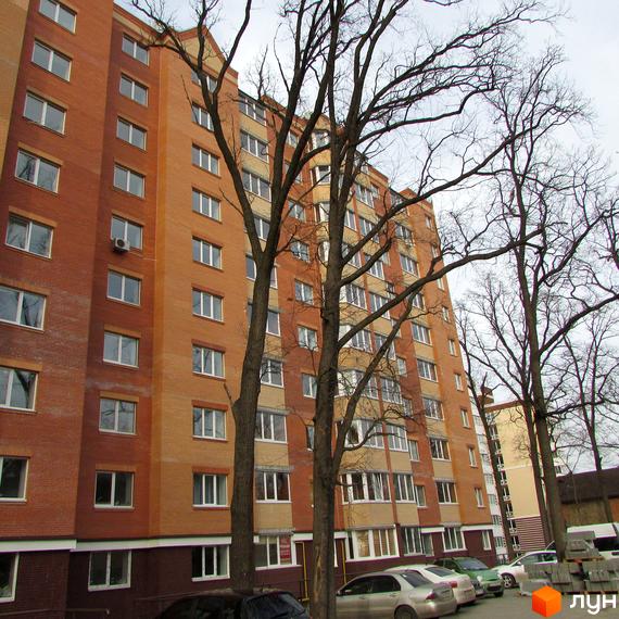 Житловий комплекс Столичний квартал: цегляний багатоповерховий будинок з білими вікнами. Навколо будинку ростуть дерева, видно припарковані автомобілі.