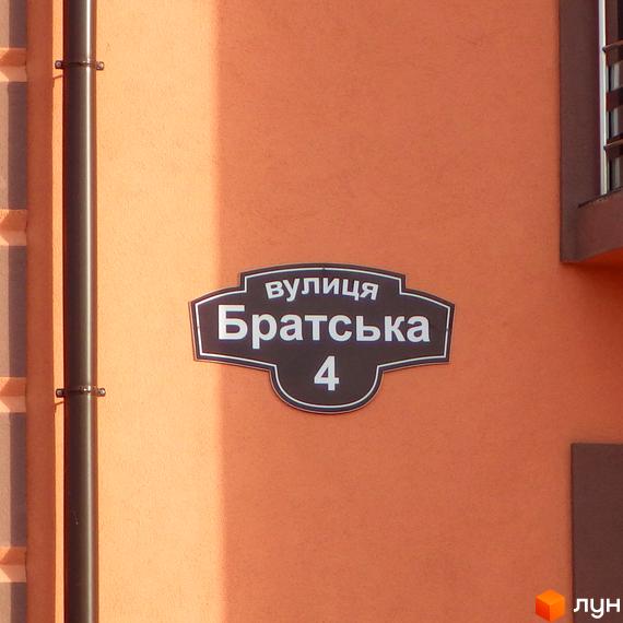 На фасаді будинку табличка з назвою вулиці Братська, 4. Новобудова Волошковий має оранжевий фасад та чорний водостічний жолоб.