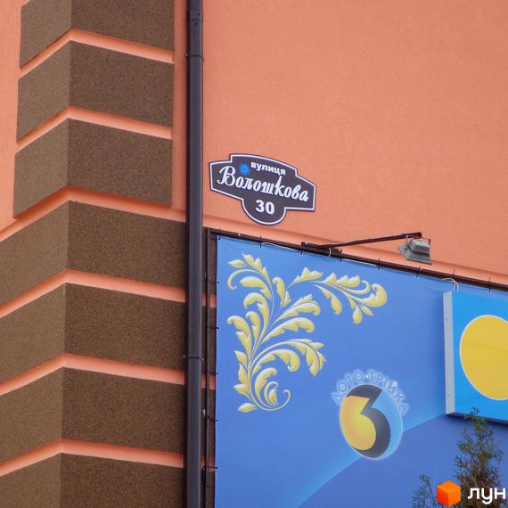 Житловий комплекс Волошковий, будинок №30. Фасад будівлі з коричневими та рожевими елементами. Поруч розташована синя білборд з жовтим орнаментом.