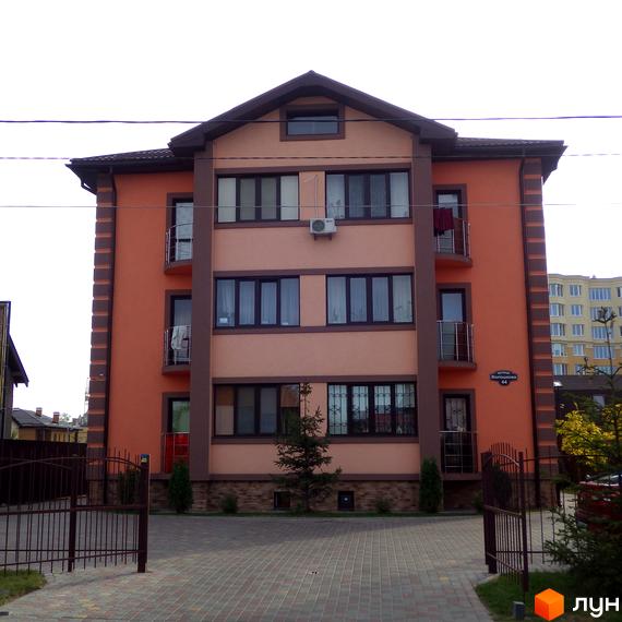 Фасад житлового комплексу Волошковий, оздоблений цеглою та штукатуркою. Прибудинкова територія з бруківкою та огорожею.