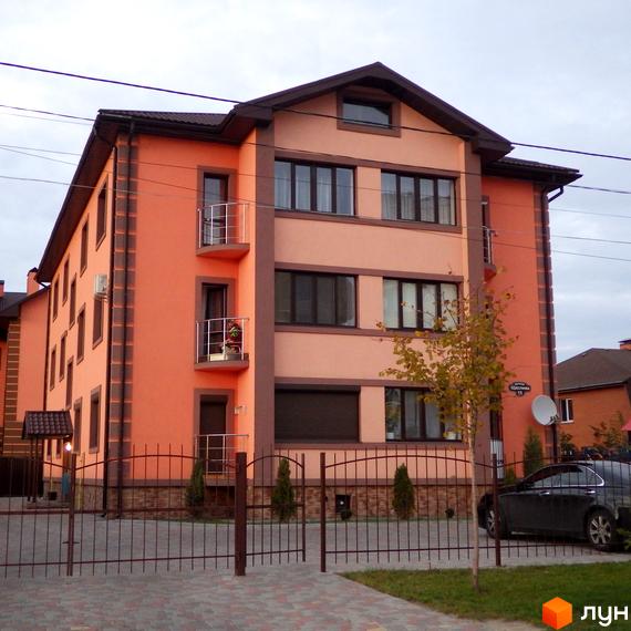 Триповерховий будинок житлового комплексу Волошковий з балконами та великими вікнами, огороджена територія з парканом та деревами.