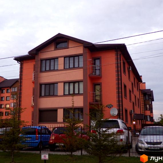 Житловий комплекс Волошковий. Зовнішній вигляд багатоповерхового будинку з оранжевим фасадом та балконами. На прибудинковій території припарковані автомобілі.