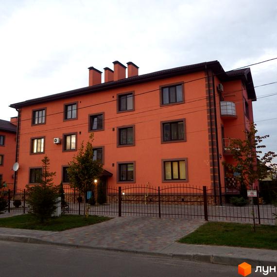 Житловий комплекс Волошковий. Фасад будинку в оранжевому кольорі з коричневими віконними рамами. Огороджена прибудинкова територія з доріжками та зеленими насадженнями.