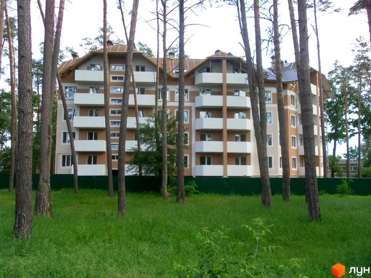 Багатоповерховий будинок ЖК Родинний серед дерев та зеленої трави. На фасаді будинку розташовані балкони, вікна та оздоблення в світлих тонах.