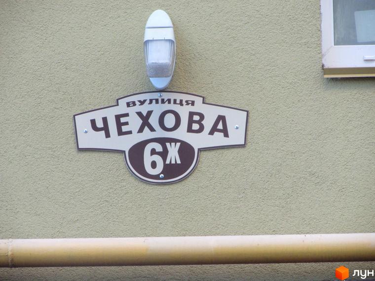 На фасаді будинку табличка з назвою вулиці Чехова та номером будинку 6Ж. Зовнішній вигляд будівлі та її адресація.