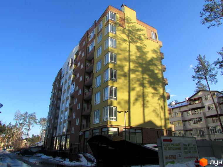 Житловий комплекс Женев'єва - фасади будівель з панорамними вікнами та балконами, оточені деревами під блакитним небом. На території видно дорогу та сніг.