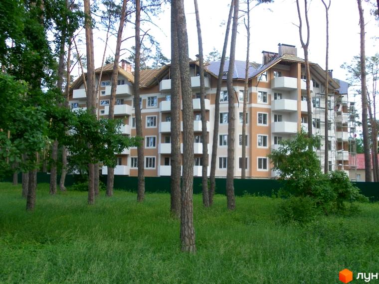 Житловий комплекс Родинний серед дерев та зеленої трави. Багатоповерховий будинок з балконами та світлим фасадом.