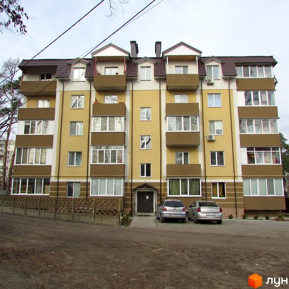 Зовнішній вигляд чотириповерхової новобудови ЖК Северинівський з жовтим фасадом та коричневими балконами. Перед будинком розташована прибудинкова територія з парковкою та парканом.