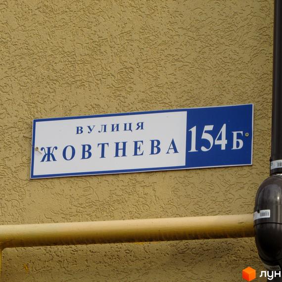 Вулична табличка з назвою вулиці Жовтнева, 154Б. Зовнішній вигляд фасаду будинку та прибудинкової території.