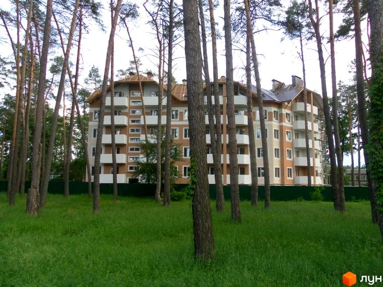 Багатоповерховий будинок ЖК Родинний серед дерев та зеленої трави. На фасаді будівлі видно балкони та вікна, а навколо - доглянута прибудинкова територія.