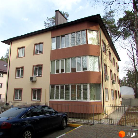 Зовнішній вигляд триповерхового будинку ЖК Привилегия з коричневими елементами та великими вікнами. Поруч припаркований синій автомобіль та огороджена територія.