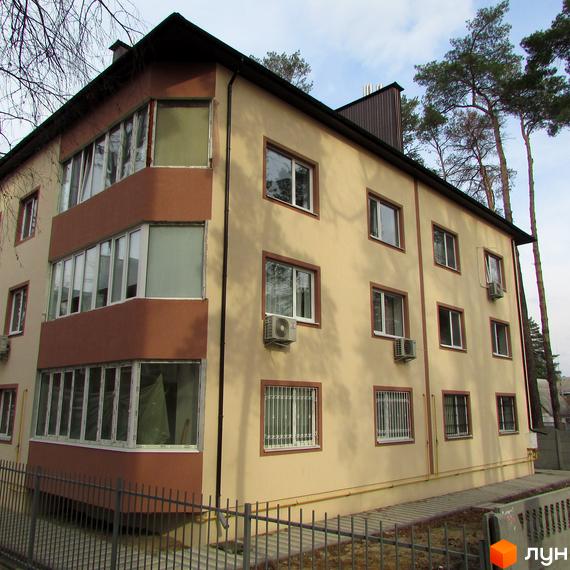 Зовнішній вигляд триповерхового будинку житлового комплексу Привилегия з коричневими елементами та кондиціонерами. Навколо будинку розташована прибудинкова територія з парканом та деревами.