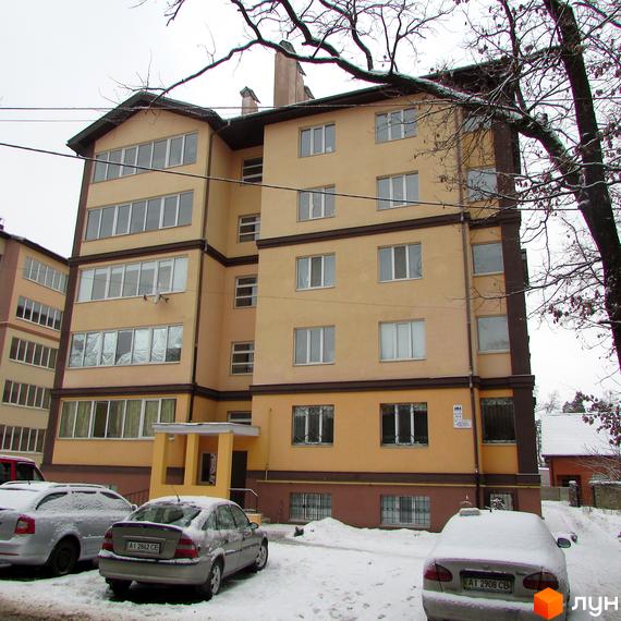 Житловий комплекс Високий: багатоповерховий будинок світло-жовтого кольору з коричневими елементами. Засніжена прибудинкова територія з припаркованими автомобілями.