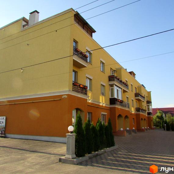 Зображення фасаду та прибудинкової території Житлового комплексу Петровский дворик. Багатоповерховий будинок жовтого кольору з балконами та зеленими насадженнями вздовж тротуару.