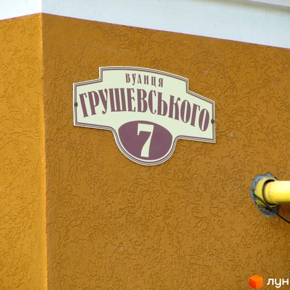 Будівельний проєкт Петровский дворик, фасад будинку з табличкою вулиця Грушевського, 7. Житловий будинок з жовтим фасадом та текстурою.