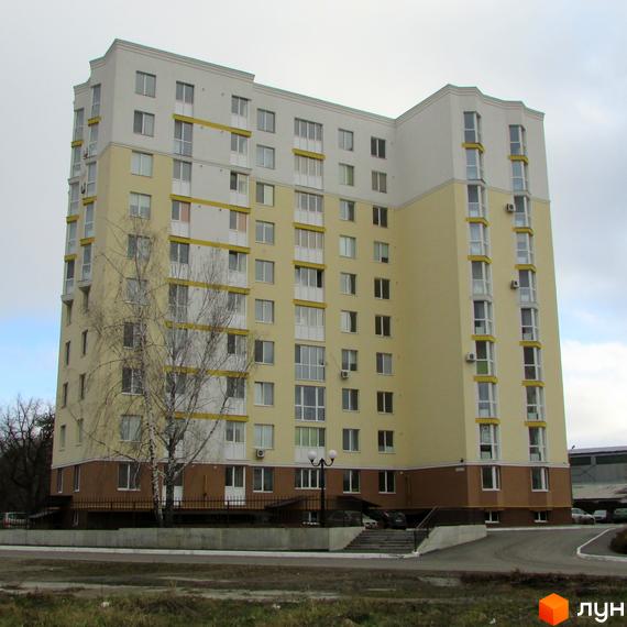 Зображення багатоповерхового будинку по вул. Тараса Шевченка, 4б. Світла будівля з великою кількістю вікон та деревами на передньому плані.