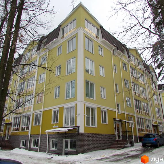 Зображення фасаду Житлового комплексу Пушкінський. Багатоповерховий будинок жовтого кольору з білими вікнами та коричневим дахом, розташований серед дерев.