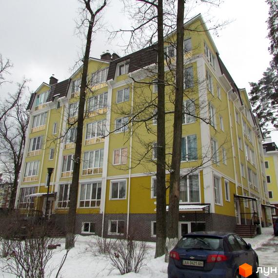 Зображення фасаду та прибудинкової території Житлового комплексу Пушкінський. Багатоповерховий будинок жовтого кольору з коричневим дахом.