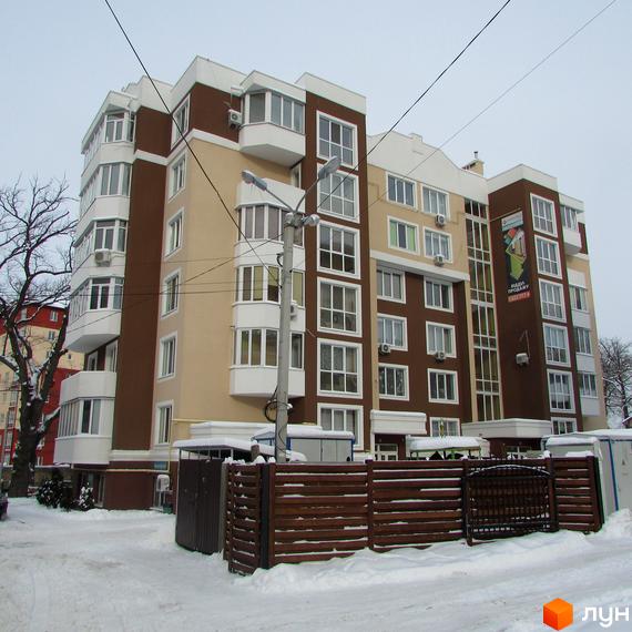 Зображення фасаду Житлового комплексу Синергія-1. Багатоповерховий будинок з коричневими та бежевими стінами, білими вікнами та балконами, огороджений парканом.