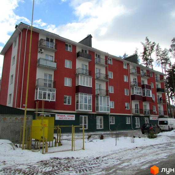Зображення чотириповерхового будинку Житлового комплексу Рильського з червоними стінами та білими балконами. На передньому плані видно сніг та газову станцію.