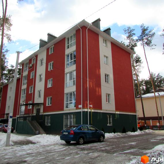 Зображення фасаду та прибудинкової території Житлового комплексу Рильського. Багатоповерховий будинок з червоно-білим фасадом та припаркованим авто.