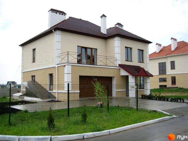 Двоповерховий будинок з коричневою черепицею та гаражем. Перед будинком зелена трава, огорожа та асфальтована дорога. Містечко котеджів Grand Villas.