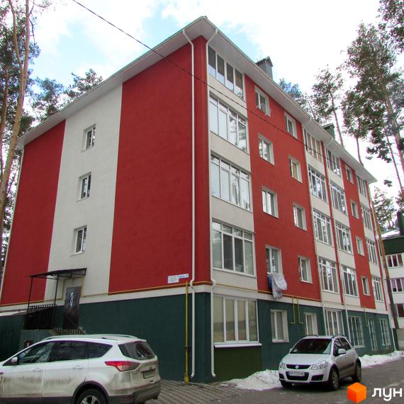 Зображення фасаду Житлового комплексу Рильського. Багатоповерховий будинок з червоно-білим фасадом та великими вікнами, поруч дерева та припарковані автомобілі.