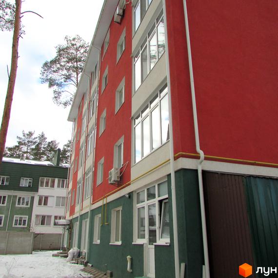 Зовнішній вигляд будинку в Житловому комплексі Рильського. Фасад червоного та зеленого кольору, великі вікна, прибудинкова територія з деревами.