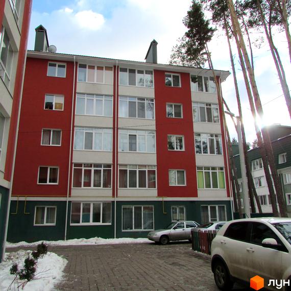 Зображення фасаду Житлового комплексу Рильського. Багатоповерховий будинок з червоними стінами та великими вікнами, прибудинкова територія з автомобілями.