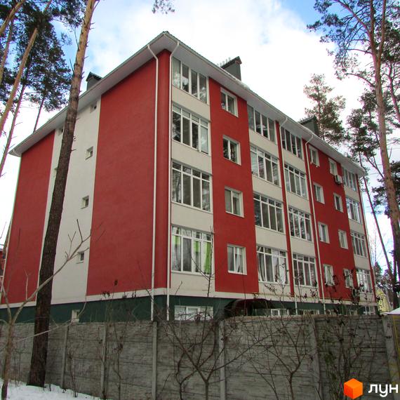 Зображення чотириповерхового будинку Житлового комплексу Рильського з червоними стінами та білими вікнами. Навколо дерева та бетонний паркан.